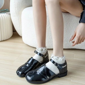 Glossy black Tabi split-toe Mary Jane shoes paired with pearl lace socks on wood floor