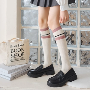 Detail of ivory knit knee-high socks with pink and black stripes paired with loafers