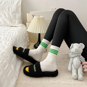 Details von Plüsch-Hausschuhen in Schwarz mit grüner Stickerei und gestreiften Socken