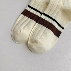 Detailed macro view of cream knitted ribbed socks featuring black and brown stripes