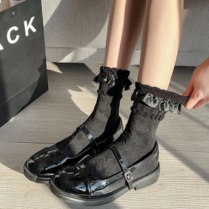 Detail of black Mary Jane shoes paired with ruffled lace socks on wooden floor