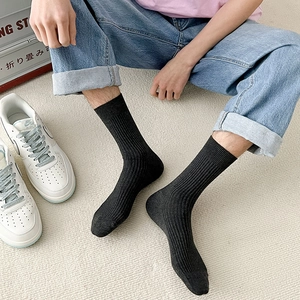 Close-up of black ribbed mid-calf socks for men paired with white sneakers and blue jeans