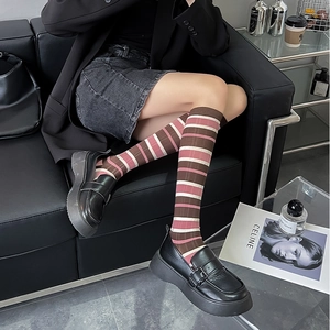 Striped knee-high socks in pink and brown tones styled with classic black platform loafers