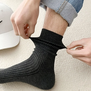 Detail showing the elastic ribbed texture of charcoal grey crew socks being stretched by hand