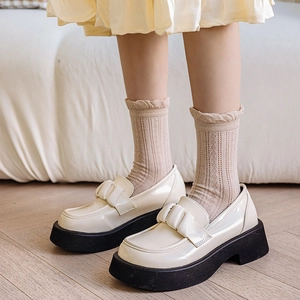 White platform loafers with glossy patent leather and bow detail in a cozy home setting