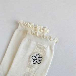Détail de chaussettes volantées blanc crème avec broderie florale et texture côtelée