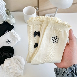 Détail de chaussettes à bord volanté avec nœud noir perlé et broderie florale
