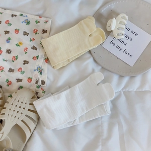 Detail of ribbed beige and white two-toe socks on a soft bed with home lifestyle decor