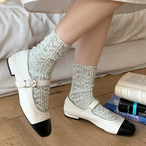 Close-up of Mary Jane flat shoes paired with floral lace socks on wooden floor