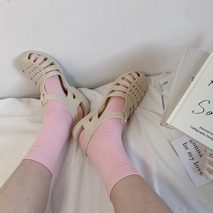 Close-up of beige hollow-out woven sandals styled with pink knit socks on a soft fabric