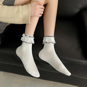 White Lolita lace socks with bow detailing on black leather background