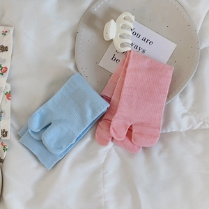 Detail of pink and blue two-toe tabi socks with soft knitted texture on white bedding