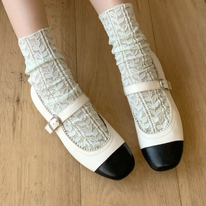 Close-up of white lace socks with hollow leaf patterns and bicolor Mary Jane shoes
