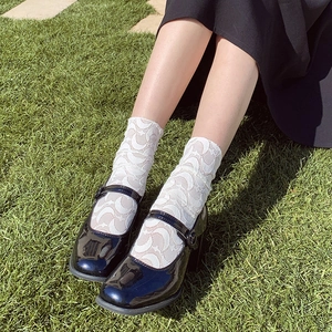 Close-up of white lace crew socks with moon patterns and black patent leather shoes