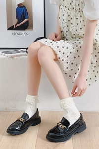 Détail de chaussettes en dentelle blanche avec mocassins noirs et chaînes dorées élégantes