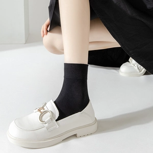 Detail of white platform loafers with horsebit buckle worn with black mid-calf socks