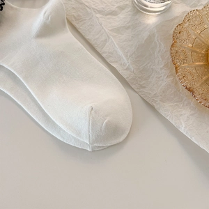 Detail of white rib-knitted socks featuring delicate black embroidery and wavy edges