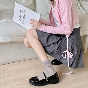 Detail of grey slouch socks paired with black Mary Jane shoes and a pleated skirt