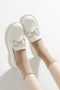 Detail of white matte loafers with gold buckle worn with khaki crew socks in minimalist style