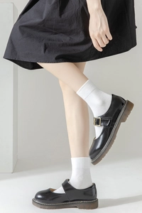 Detail of black Mary Jane shoes with platform sole and yellow stitching on white socks