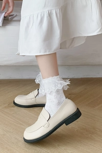 Gros plan sur des chaussettes blanches à volants en dentelle et mocassins beiges
