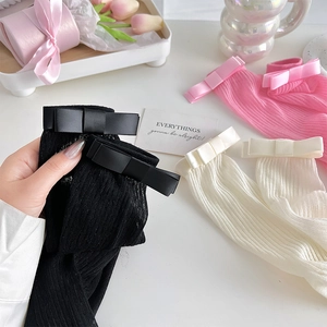 Détail de chaussettes côtelées avec nœuds en satin noirs, blancs et roses