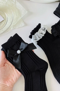 Détails de chaussettes noires à côtes avec nœuds en satin, perles et dentelle