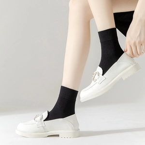 White platform loafers with metal buckle worn with black mid-calf socks for women