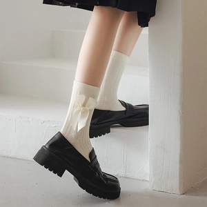 Détail de chaussettes torsadées blanches avec nœuds satinés et perles et mocassins noirs