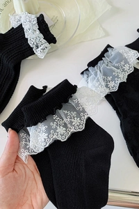 Détail de chaussettes mi-mollet noires côtelées avec bordure en dentelle blanche et broderie