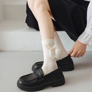 Détail de chaussettes blanches en maille torsadée avec nœud en soie et perle