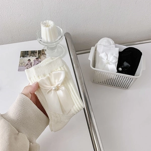 Détail du tricot de chaussettes blanches avec un grand nœud en satin et une perle