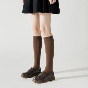 Gros plan de chaussettes hautes marron à côtes, mocassins marron et jupe plissée noire