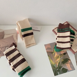 Detail view of beige ribbed crew socks with retro green and brown stripes on a white table