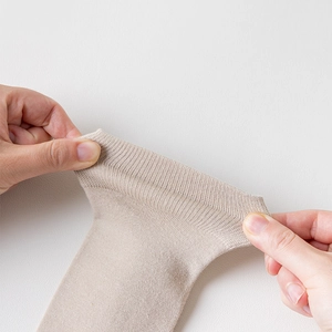 Gros plan du revers élastique d'une chaussette en tricot beige montrant son élasticité