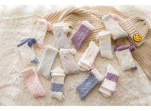 Flat lay of colorful coral fleece socks with pompoms on cozy plush blankets for winter