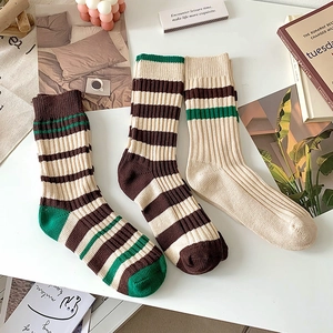 Close-up of three pairs of beige and brown striped cotton mid-calf socks on a white desk