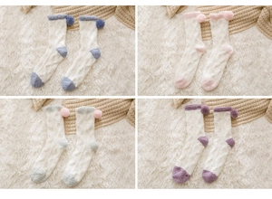 Detail of coral fleece socks in four candy colors with decorative pom-poms on plush rug