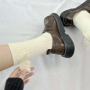 Detail of cream-colored ribbed socks featuring cute white wings paired with brown loafers