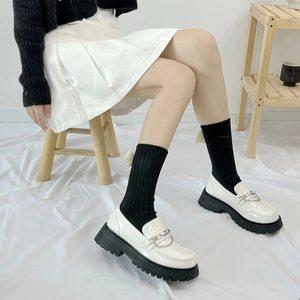 Detail of white platform loafers with silver chain paired with winged black socks