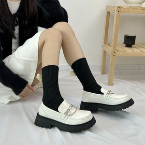 Close-up of white platform loafers with silver chain and black vertical striped socks