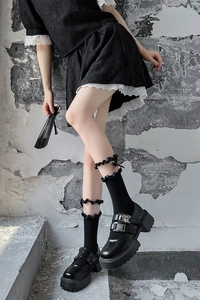 Gros plan de chaussures Mary Jane noires vernies à double bride et chaussettes à froufrous