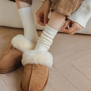 Close-up of chestnut suede slippers with white plush lining and vertical striped wool socks