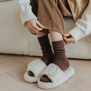 Detail of warm wool socks with vertical stripes and white plush slippers for winter comfort