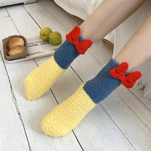 Detail of coral fleece socks with 3D red bow on cozy blue and yellow plush fabric