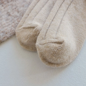 Macro detail of beige wool blend socks showing thick vertical rib texture and reinforced toe