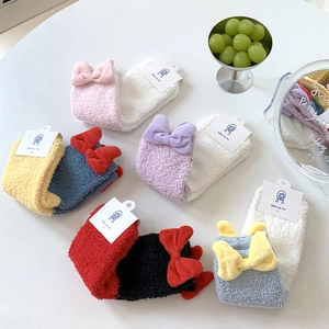 Detail view of colorful coral fleece socks featuring large decorative plush bows