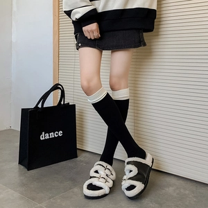 Close-up of black plush slides with white faux shearling trim and metal buckles