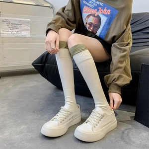 Detail of white knee-high socks with olive green ribbed cuffs and canvas shoes