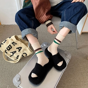 Detail van groen en bruin gestreepte geribbelde sokken met zwarte pluche slippers